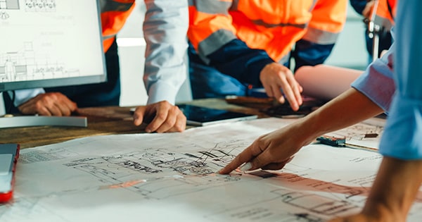 A construction crew huddles around an architectural plan