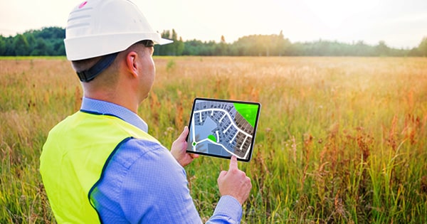 A man holds a tablet-based development plan in the middle of a field