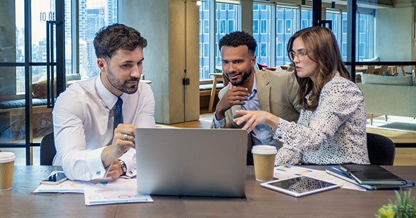 Colleagues huddle around a laptop within an office